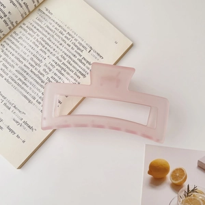 Détail macro d'une grande pince à cheveux carrée rose mat posée sur un livre ouvert