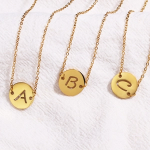 Détail de trois colliers en acier inoxydable doré avec pendentifs ronds gravés A, B et C