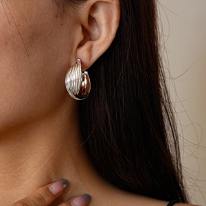 Close-up of model wearing textured silver C-shaped clip-on earrings with ribbed metal finish