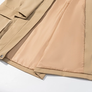 Détail du trench-coat kaki avec bouton métallique et coutures de précision sur l'ourlet