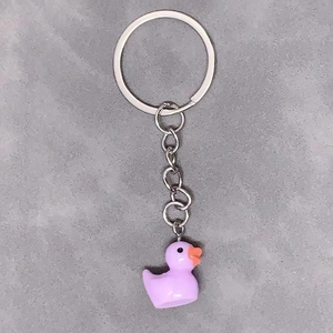 Minimalist purple resin duck keychain with silver metal ring on grey textured background