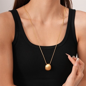 Close-up of golden oval matte pendant on a long chain necklace worn on black top