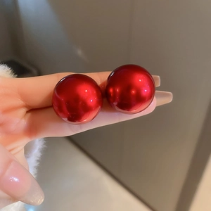 Macro detail of glossy red spherical stud earrings held between fingers for size display