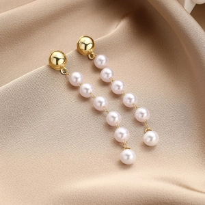Macro shot of long drop pearl earrings on champagne silk background for weddings