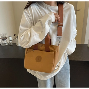 Détail d'un sac cabas en toile jaune moutarde avec bandoulière marron porté par une femme