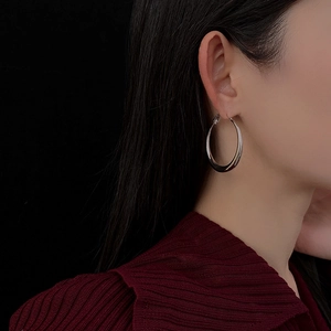 Close-up of model wearing silver oval hoop earring against a minimalist black background