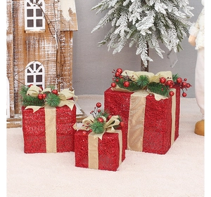 Three red Christmas gift boxes with gold ribbons and pine needles on a cozy rug