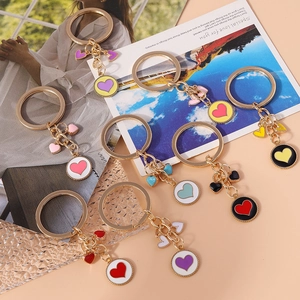 Colorful enamel heart pendants on gold keychains showcased on a decorative pink background
