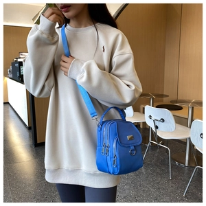 Detail of royal blue nylon crossbody bag with multi-zipper layers worn by model