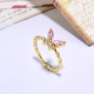 Close-up of gold butterfly ring with pink crystals and twisted band detail on vintage paper