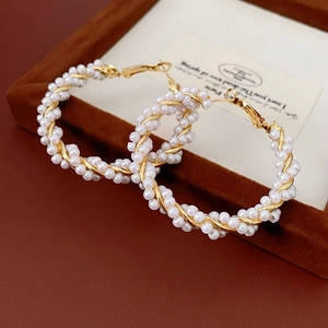 Detailed close-up of golden twist hoop earrings with white pearls on brown velvet