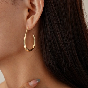 Close-up of polished golden oval hoop earrings on a model showing smooth metallic finish