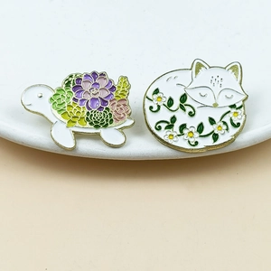 Detailed enamel pins featuring a turtle with succulents and a fox curled with flowers