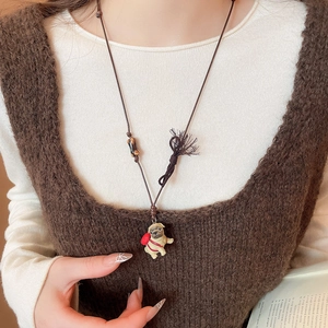 Close-up of a pug ceramic pendant with wax rope, wooden beads, and tassel detail on a necklace