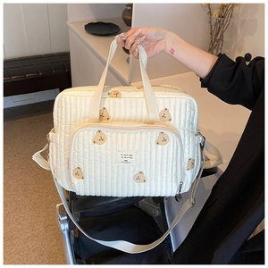 Sac à langer matelassé beige avec broderie d'ours accroché sur une poussette bébé