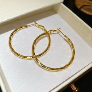 Detail of twisted 14k gold plated hoop earrings with glossy texture in a white jewelry box