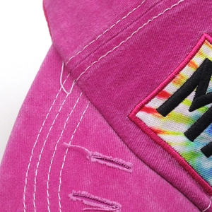 Close-up of distressed cotton texture and tie-dye embroidery patch on a pink baseball cap