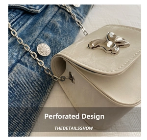 Detail of creamy white crossbody bag with silver butterfly clasp on denim background