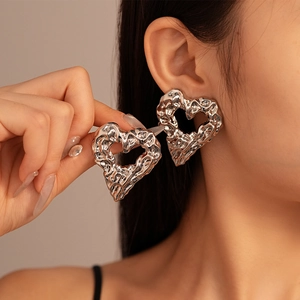 Model wearing large silver liquid metal heart earrings with a textured lava design