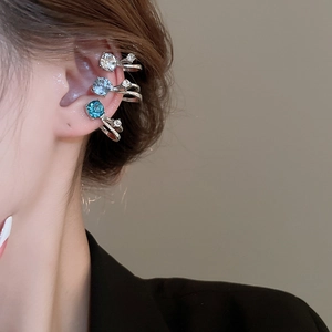 Détail de trois ear cuffs argentés avec des strass étincelants bleus et blancs