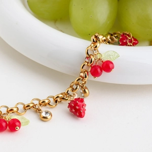 Detail of gold chain bracelet with red strawberry, cherry charms and clear crystals