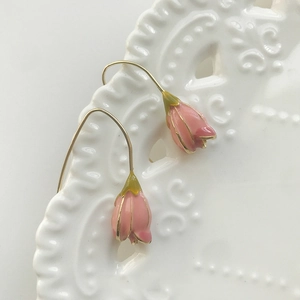 Detailed close-up of pink tulip enamel earrings hanging on a white decorative ceramic dish