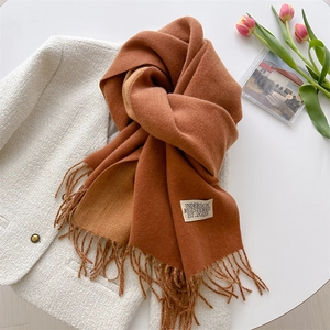 Detail van bruine kasjmier-stijl sjaal met franjes op een wit tweed jasje