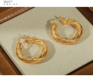 Detailed macro view of golden twisted hoop earrings on a soft grey velvet display tray