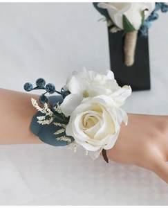 Detail of white rose wrist corsage with blue berries and greenery for wedding guests