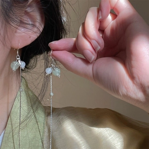 Detail view of long tassel earrings with light green beads and silver chains on a model