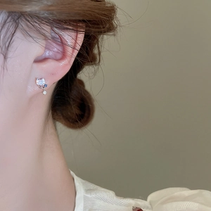 Close-up of heart-shaped zircon earring with blue accent stone on a model's ear