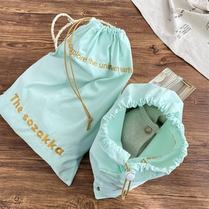 Close-up of mint green drawstring storage bags with gold embroidery on wooden background
