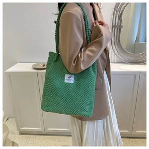 Close-up of green knit tote bag with 'Youneedthisone' label worn with a blazer