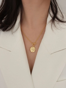 Macro detail of a 925 silver gold coin necklace with T-bar toggle and hammered texture