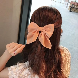Large orange satin bow hair clip styled on wavy brown hair for a Japanese JK aesthetic
