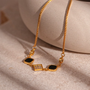 Macro detail of gold plated box chain bracelet with black zircon geometric pendants