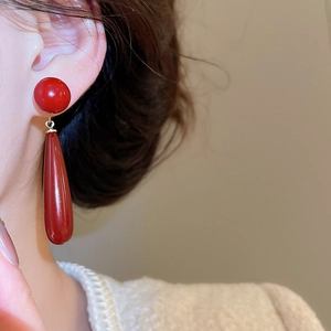 Close-up of red teardrop pearl earrings worn by a model in a cozy white sweater