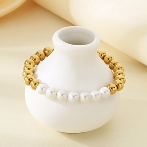 Détail d'un bracelet en perles et acier plaqué or 18K sur un vase décoratif en céramique
