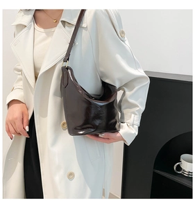 Detail of dark brown glossy patent leather hobo bag worn with a white trench coat