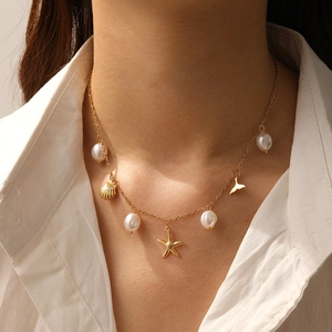 Close-up of golden necklace with white pearls, starfish, seashell, and mermaid tail charms