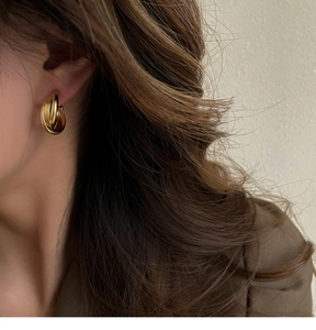 Détail d'une boucle d'oreille torsadée dorée portée par un mannequin avec finitions satinées