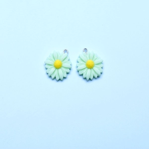 Macro view of two light green resin daisy flower charms with yellow centers and silver loops
