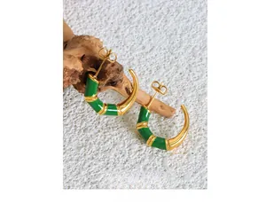 Detail of bamboo-style C-shaped gold earrings with green enamel on a wooden stand