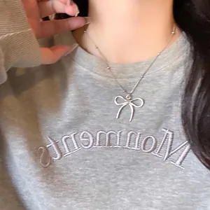 Collier nœud argenté avec chaîne à perles porté sur un fond de sweat-shirt gris