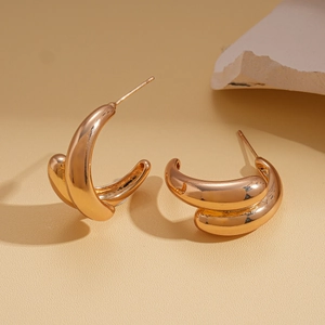 Detailed view of gold plated C-shaped drop earrings on a minimalist stone background