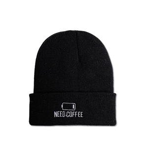 Close-up of black knit beanie with white Need Coffee and low battery embroidery