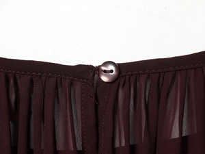 Détail macro du tissu en mousseline bordeaux avec col volanté et fermeture bouton