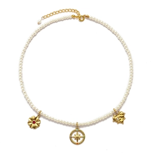 Detail of gold pearl necklace with red flower, star compass, and heart charms