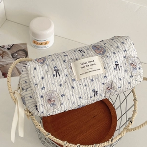 Close-up of quilted floral bear cosmetic bag in a wire basket with skincare props