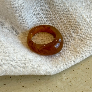 Close-up of a minimalist amber resin oval ring on soft white crinkled fabric texture